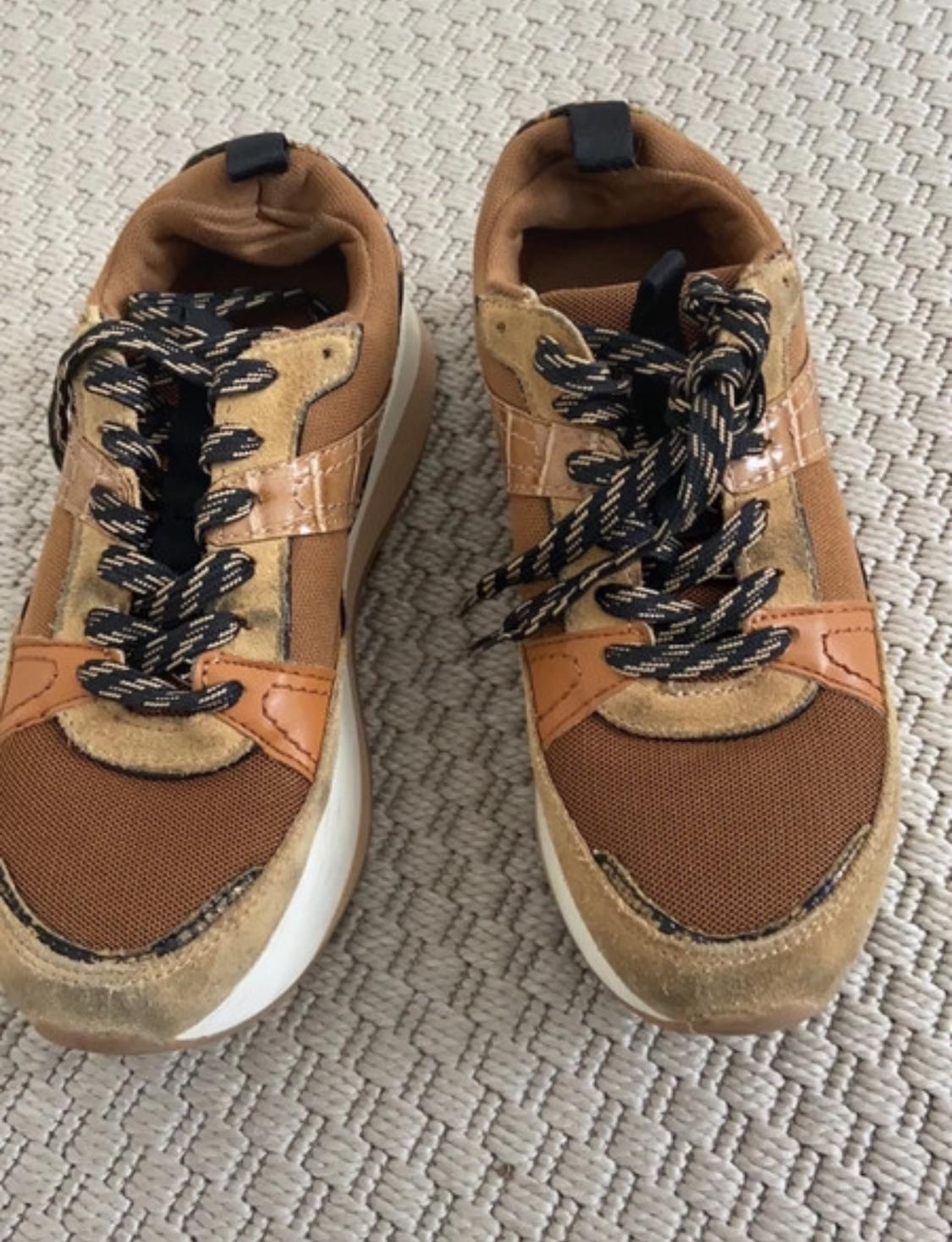 Detail of brown trainers with black laces and white soles.