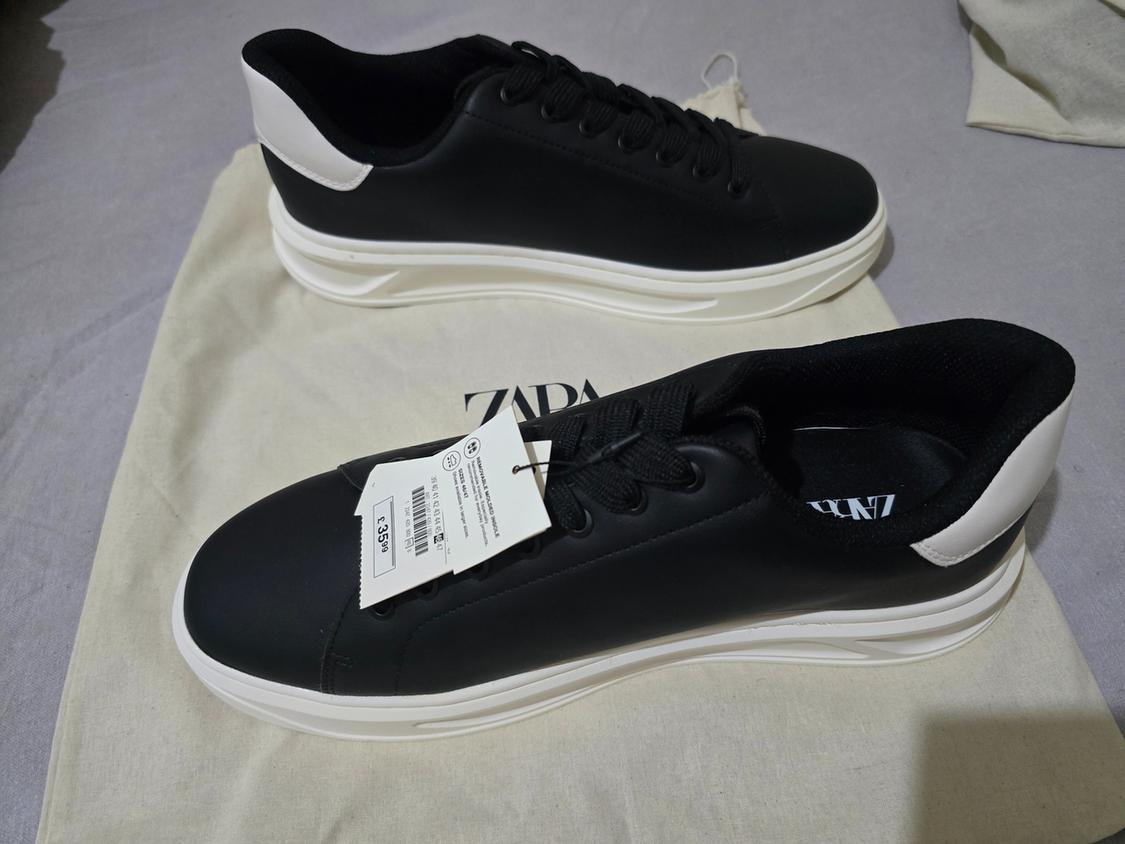 Black trainers with white soles and heels on a canvas bag. Text: ZARA, REMOVABLE MOLDED INSOLE, £35.99.