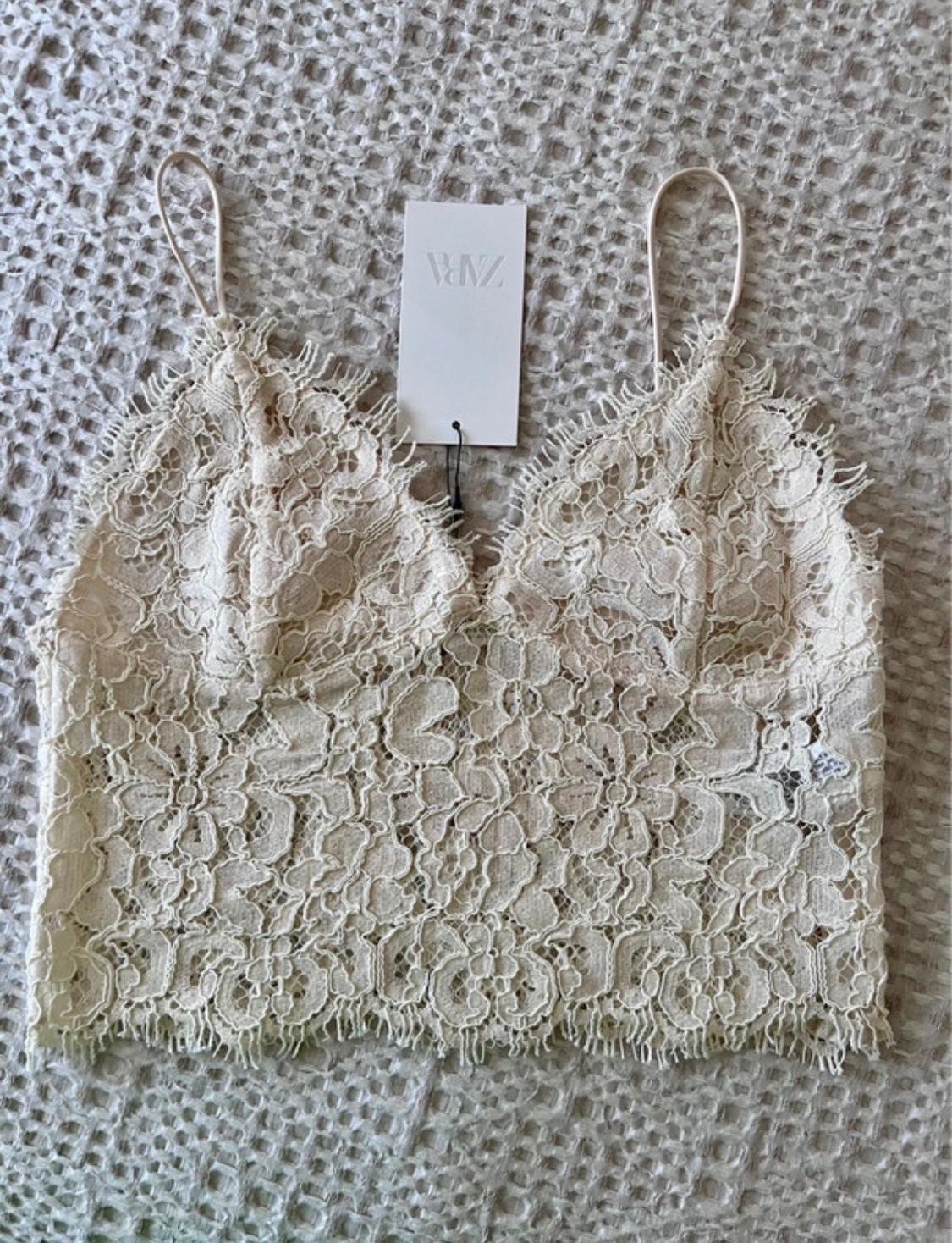 Cream-coloured lace crop top with spaghetti straps on a textured blanket. Tag with the text ZARA.