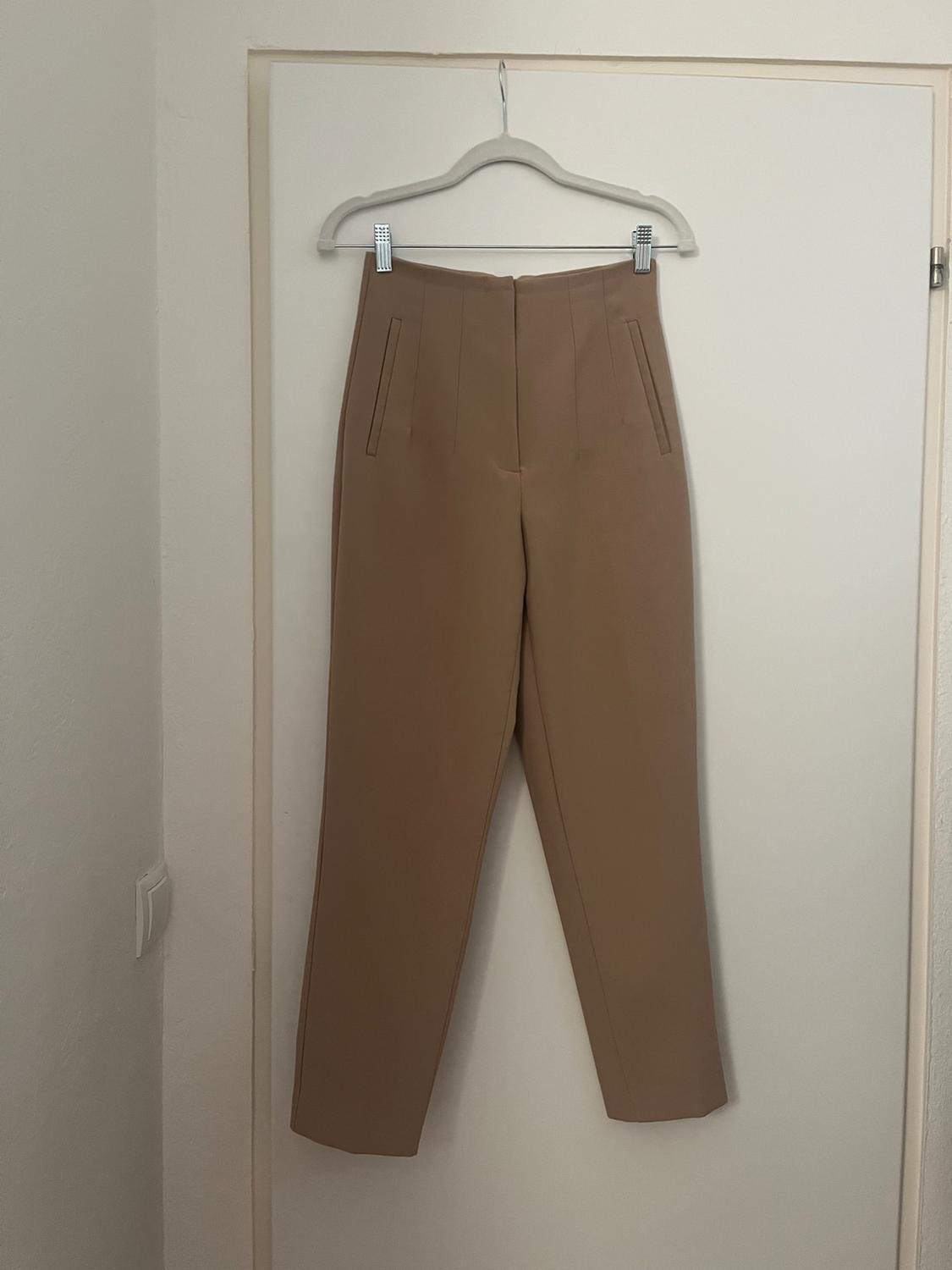 Beige trousers hanging on a white hanger over a white door. Minimalist and simple atmosphere.