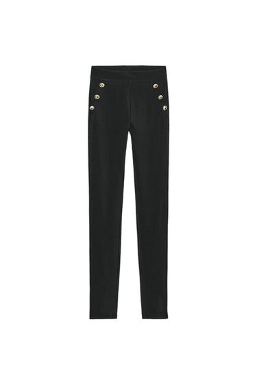 Front view of black leggings with elasticated waistband and faux pockets decorated with embossed metallic buttons.