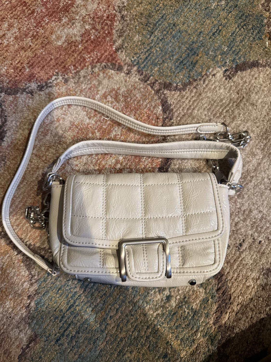 Small white bag with square texture and metal buckle on a multicolored rug with circular patterns.