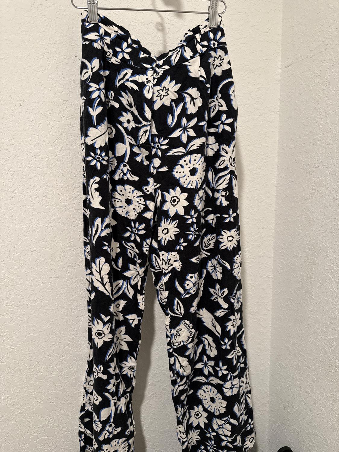 Trousers hanging with black and white floral print on a black background, on a white wall.