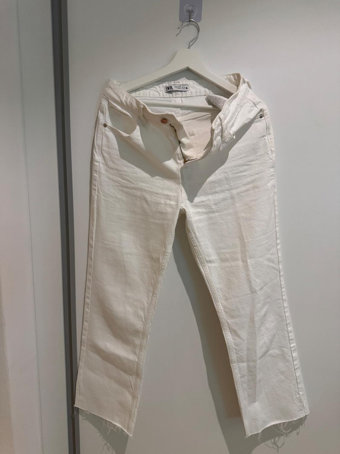 Front view of white trousers with side pockets and frayed hems.