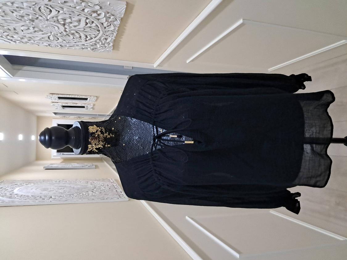 Mannequin in a sheer black dress with gold details on the neckline, in a hallway with white panelled wall decor.