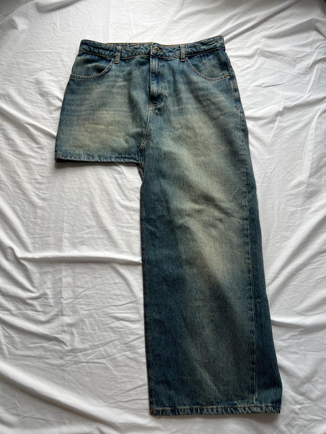 Asymmetrical blue denim jeans over wrinkled white fabric. Creative design that stands out for having one short leg and the other long and wide.