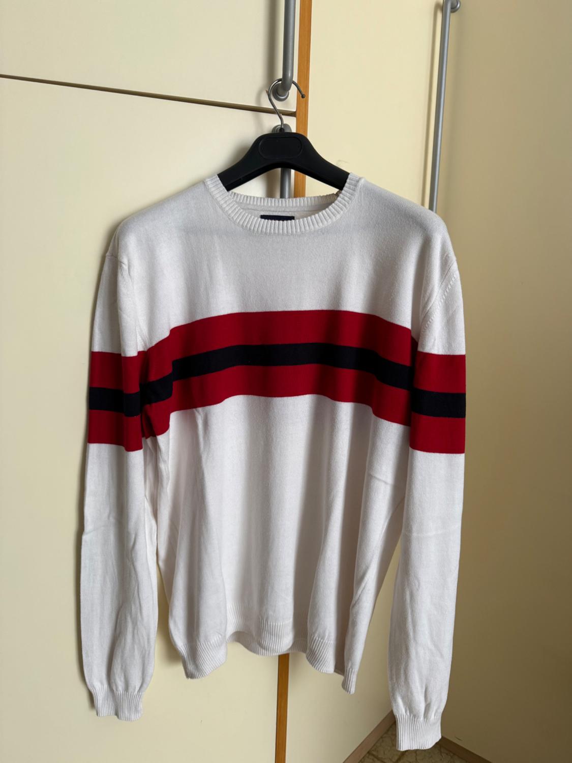 White jumper with horizontal red and black stripes, hanging on a black hanger in front of a beige wardrobe.