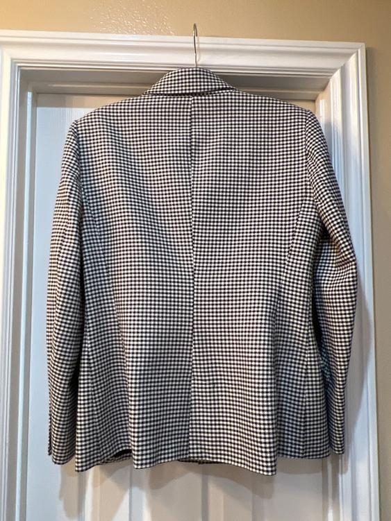 Black and white plaid jacket hanging on a white door. The jacket has lapels and long sleeves.