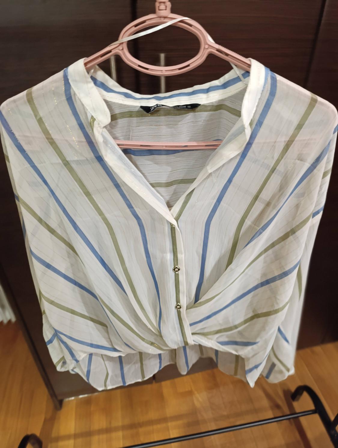 Blue and green striped blouse hanging on a pink hanger. Dark wooden background and parquet flooring.