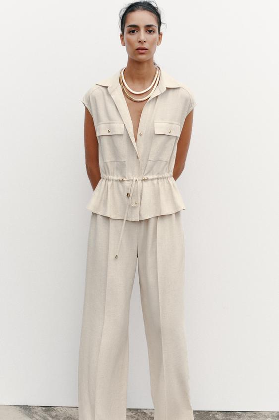 Světle béžový overal s límečkem košile, bez rukávů, přední kapsy s klopou, elastický pas a široké nohavice.