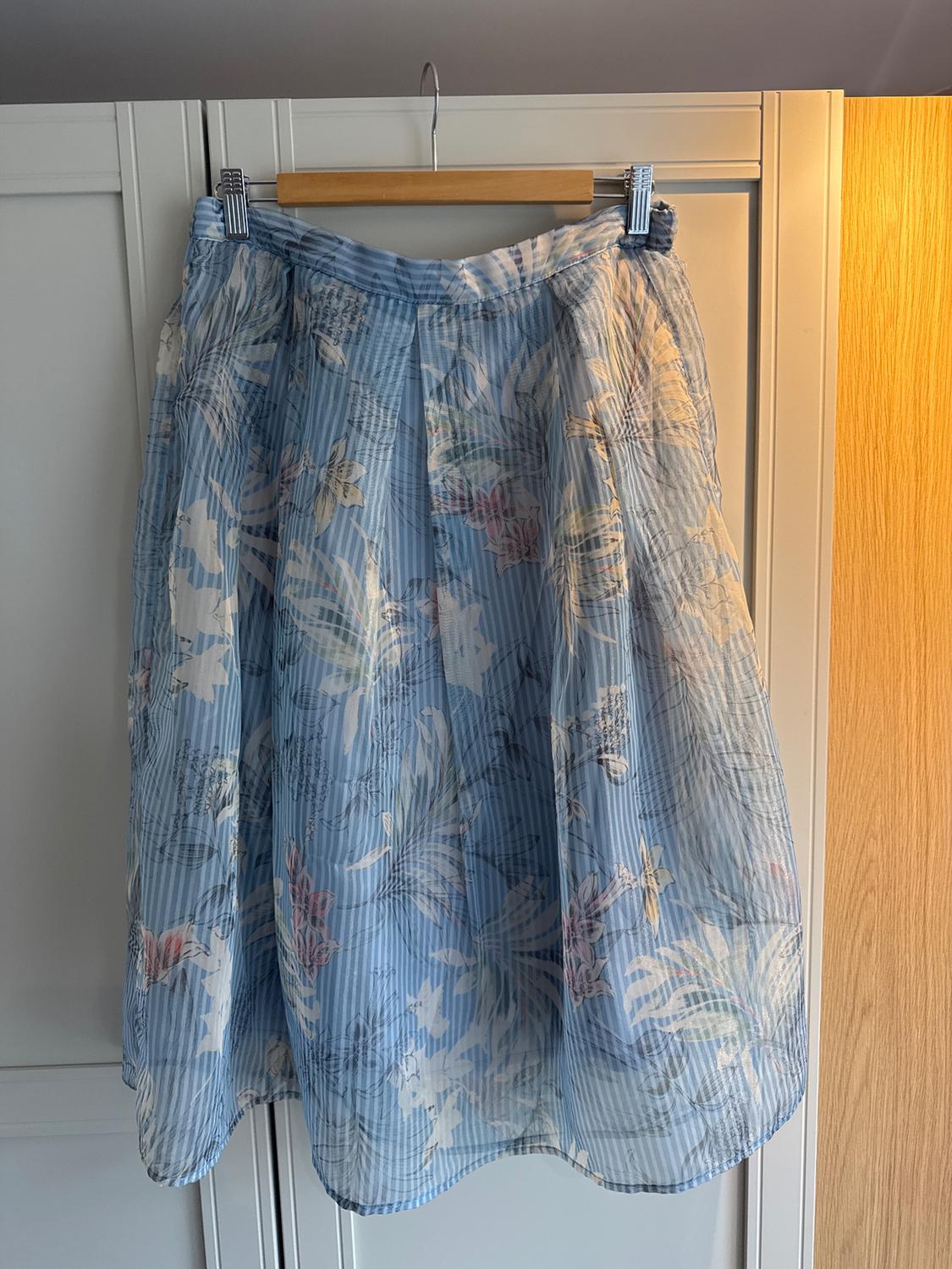 Blue skirt with a floral and vertical stripe print, hanging on a wooden hanger in front of a white wardrobe.