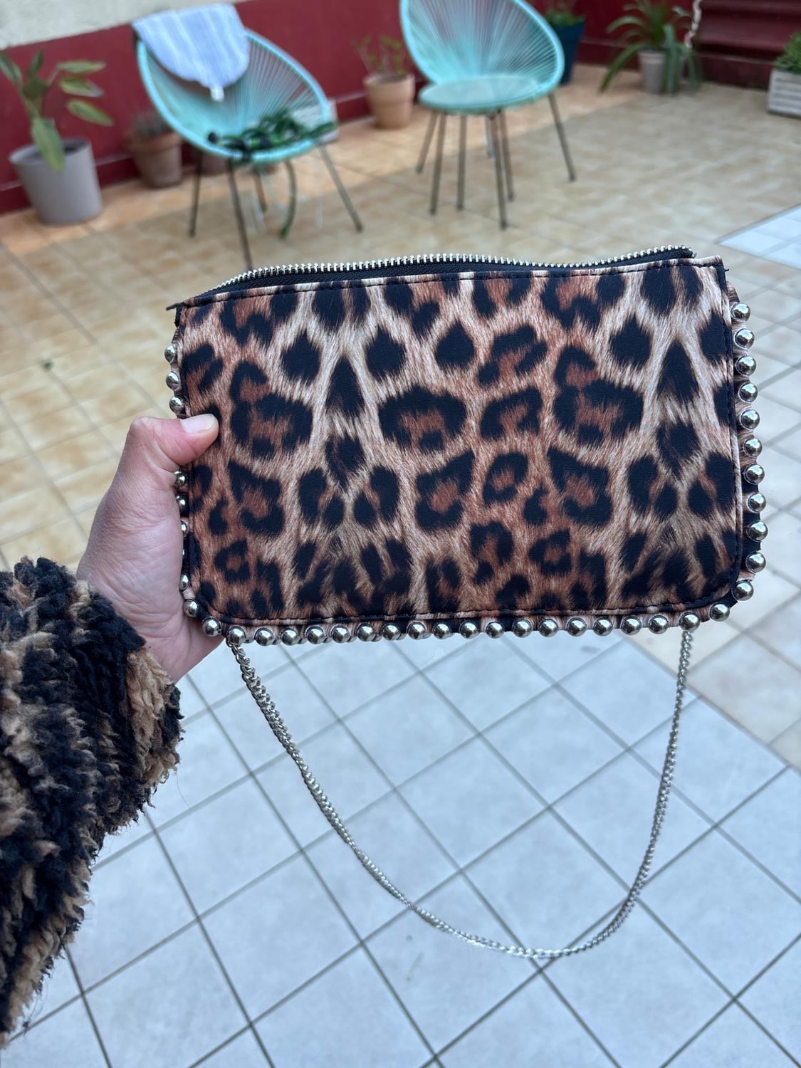 Leopard print handbag with silver chain, held by a person in a courtyard with chairs and plants.