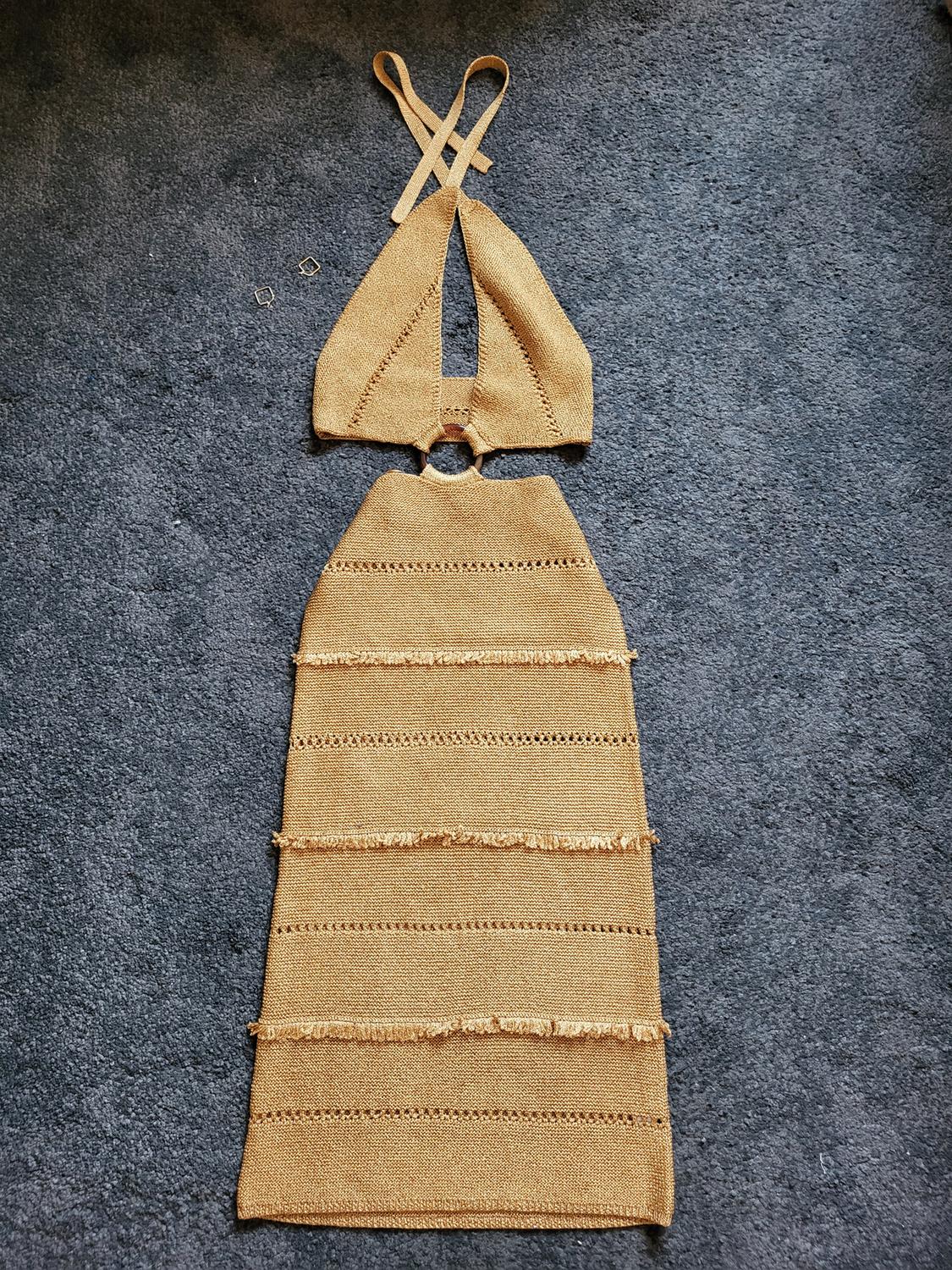 Brown knitted dress with crossover straps and fringe details, on a grey rug.