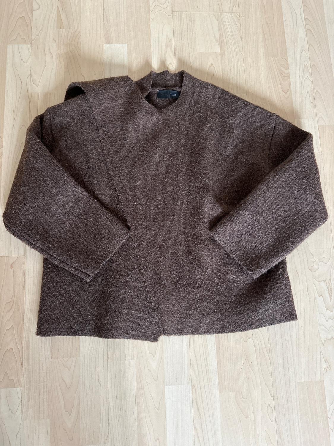 Brown wool jumper with a loose fit and long sleeves, placed on a light wooden floor.