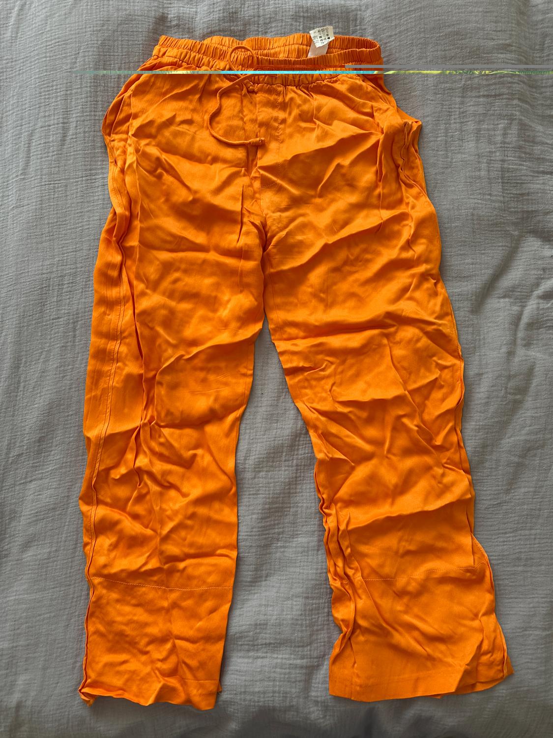 Creased orange trousers with an elasticated drawstring waist, laid flat on a grey surface.