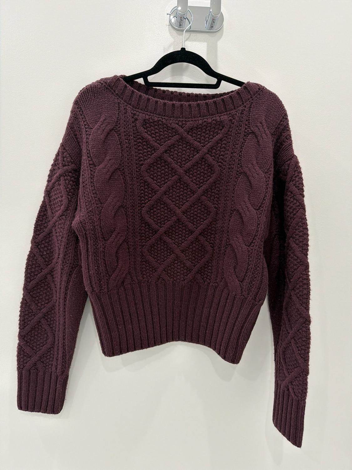 Chunky-knit burgundy sweater with a cable-knit pattern and crew neck, hanging on a black hanger against a white wall.