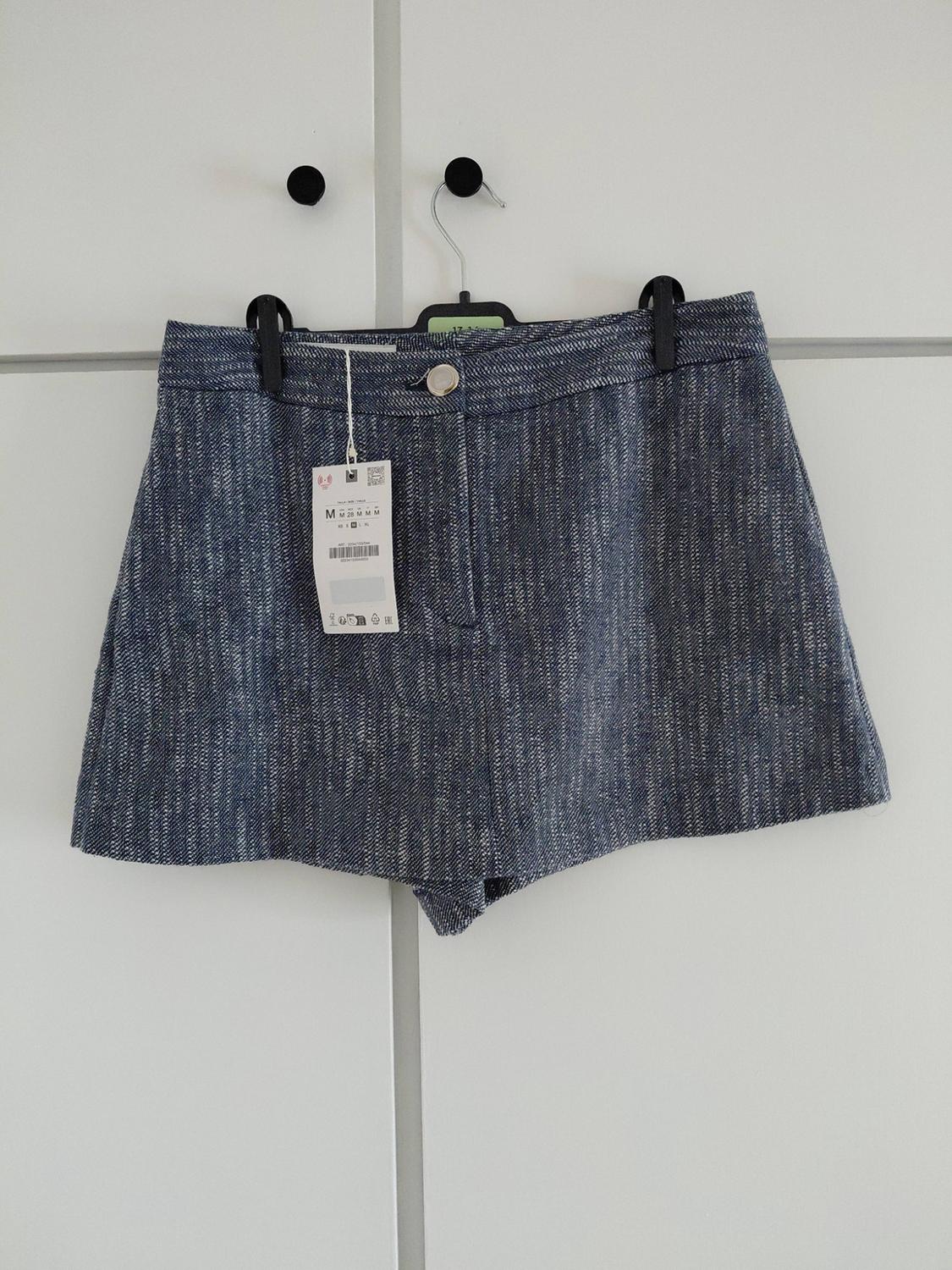 Textured blue shorts hanging on a black hanger above a white wardrobe. They have one button and a label bearing the text M.