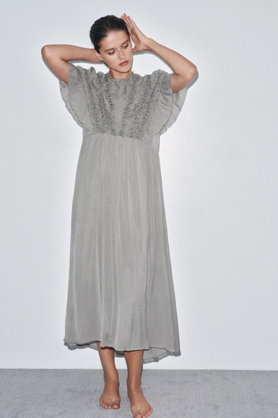 Šedé midi šaty s kulatým výstřihem, krátké rukávy s volánky, výšivka s uzlíkovým vzorem a aplikace šperků.