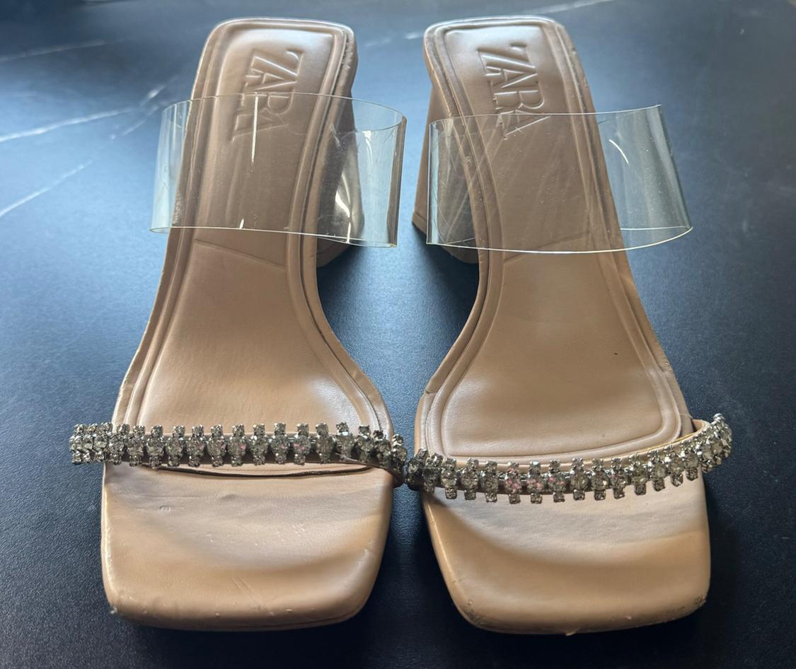 Front view of sandals with a square heel, clear strap, and diamante embellishment on the toe.