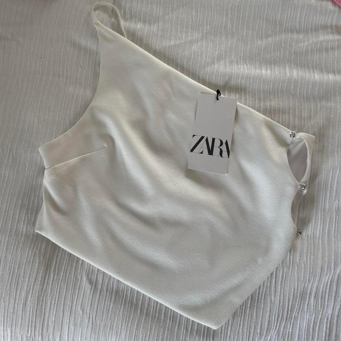 White vest top on a textured white surface, with a hang tag that reads "ZARA".