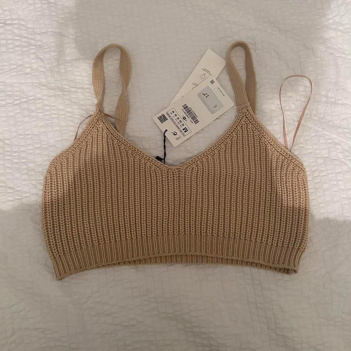 Beige knitted top with straps on a white bedspread. Visible labels with size and price information.