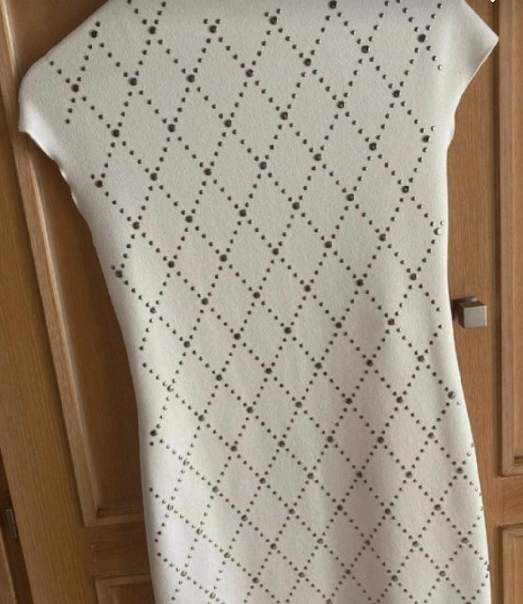 White dress with diamond cut-out pattern, hanging over a light wooden door.