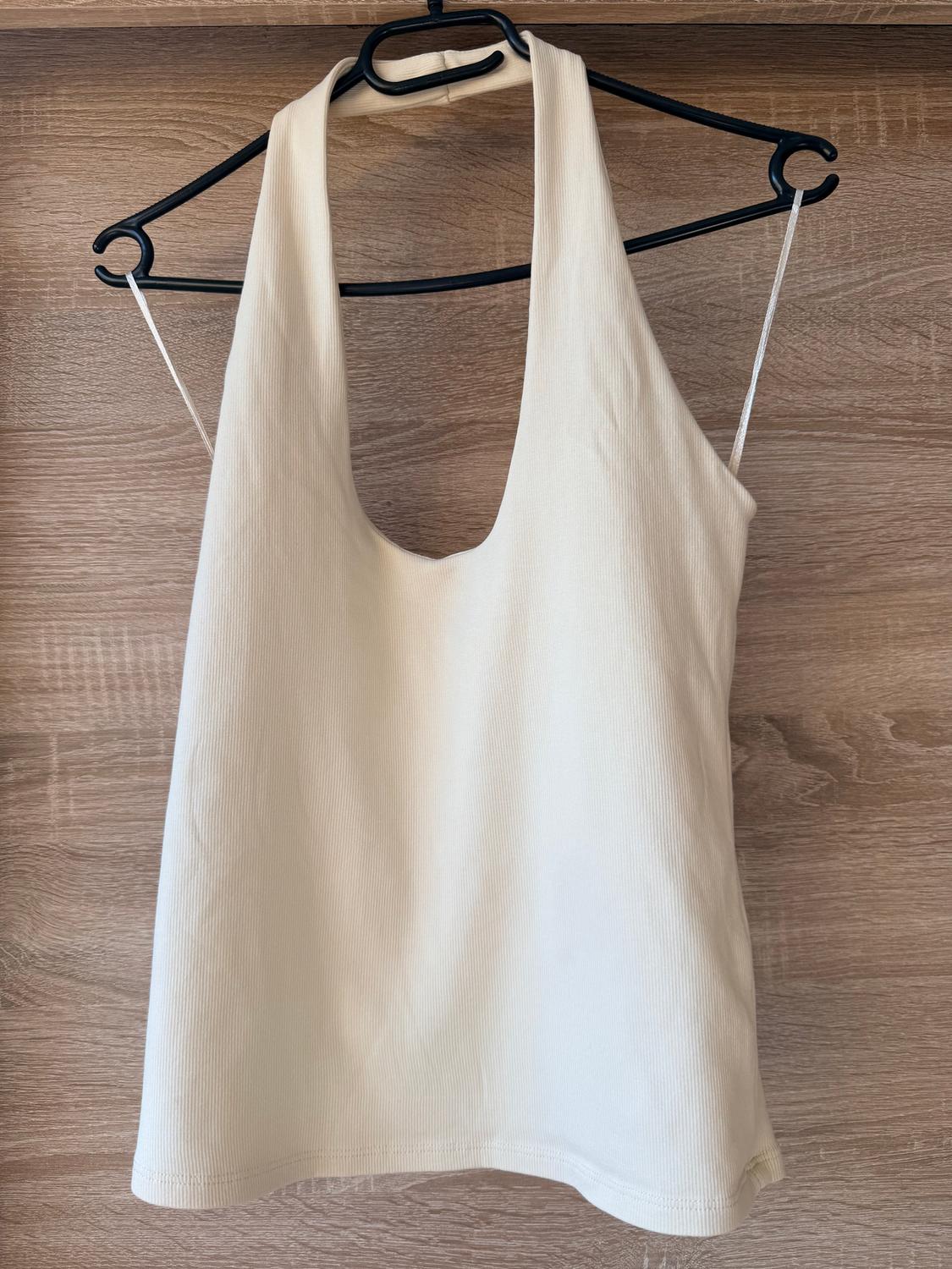 Cream-coloured vest top hanging on a black hanger against a light wooden background.