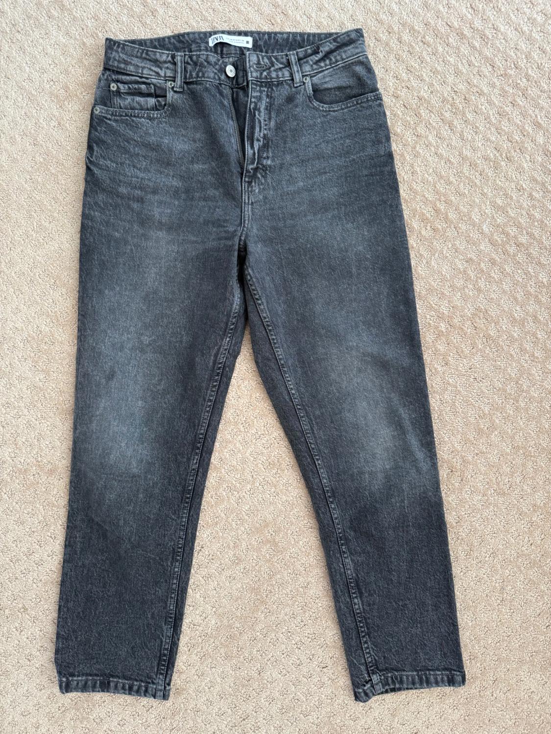 Straight-cut grey jeans on a beige rug. Visible label on the waistband with text.