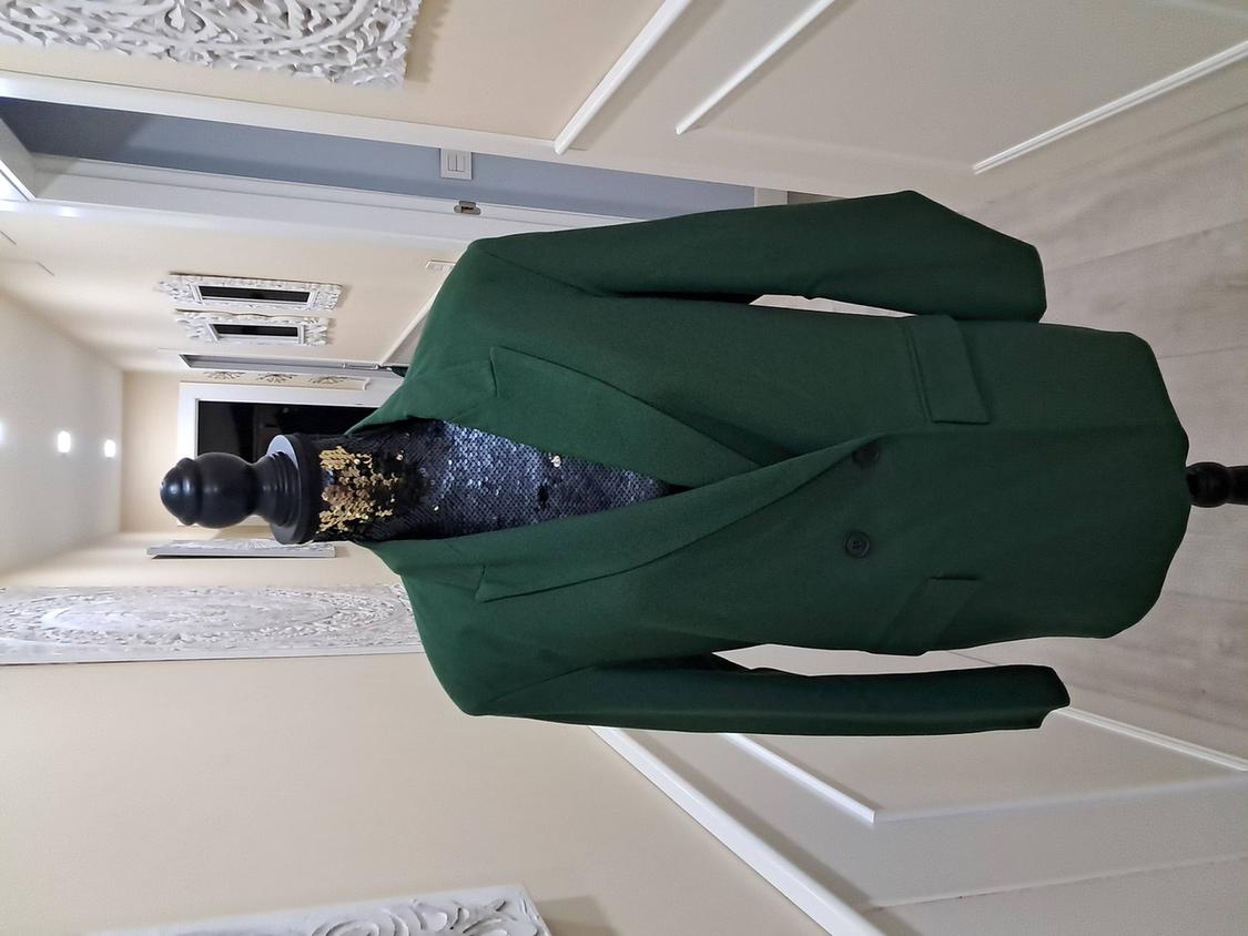Mannequin in a dark green jacket over a black and gold sequin dress in a hallway with white wall decor.