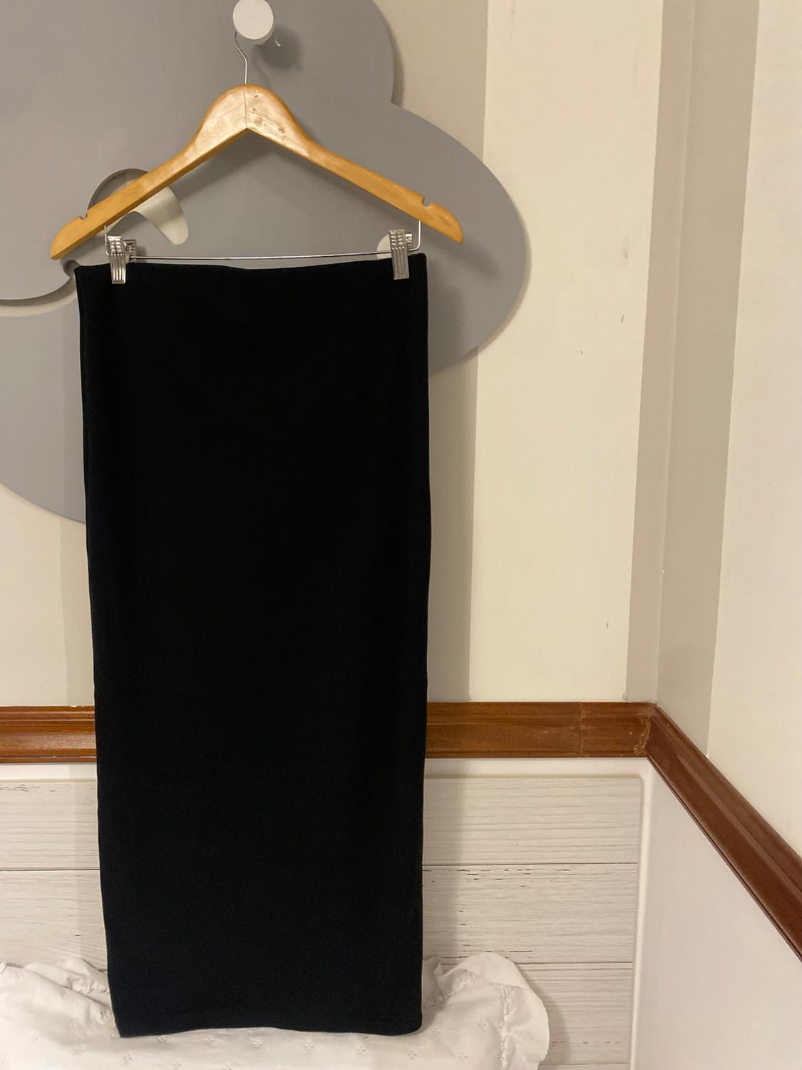 Black skirt hanging on a wooden hanger against a light background with wooden accents. Minimalist and elegant atmosphere.