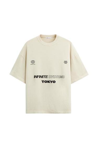 Μπεζ μπλουζάκι με μαύρο κείμενο "INFINITE SYSTEMS TOKYO", λογότυπο υδρόγειου σφαίρας και μικρό κείμενο "space est." και "east coast 4am".