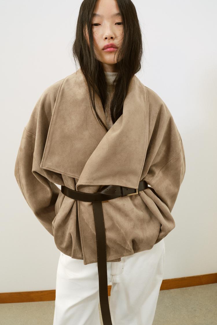 St�edn� detail tmav� velbloud� bundy s ob�lkov�m l�mcem a �ern�m p�skem, dlouh�mi ruk�vy a skryt�mi bo�n�mi kapsami.