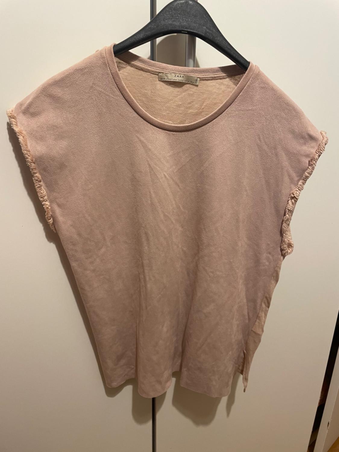 Front view of a beige sleeveless t-shirt with a round neck and frayed hem.