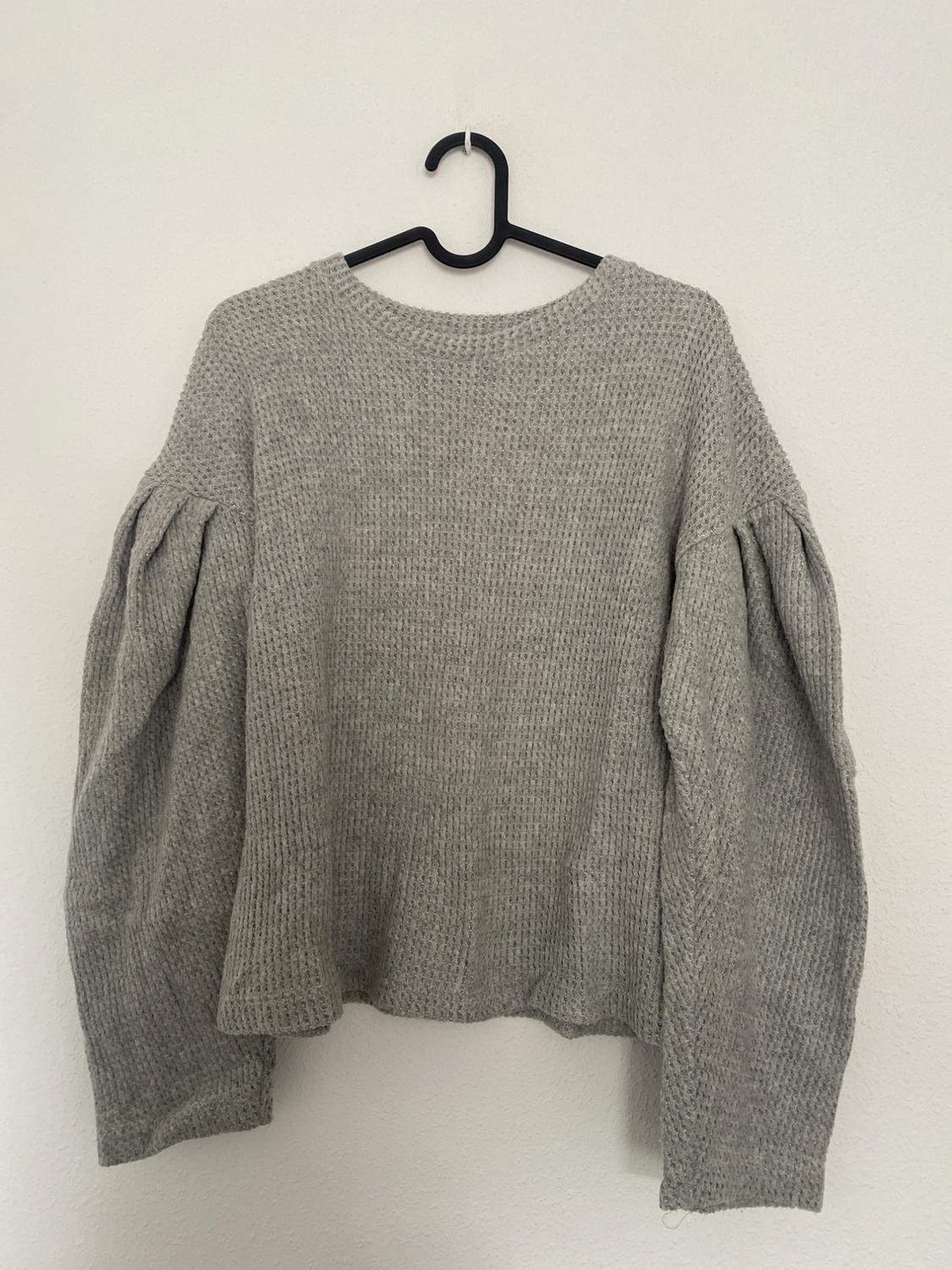 Front view of a grey jumper with long sleeves and a knit texture.