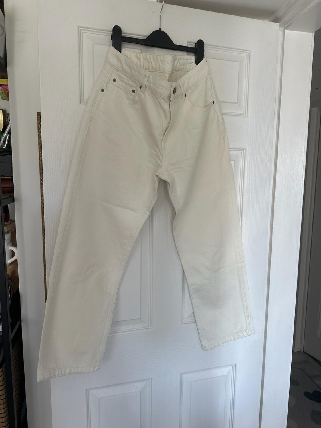 White straight-leg jeans hanging from a black hanger on a white door in a casual home setting.