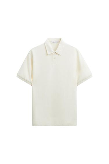 White short-sleeved polo shirt with a classic collar and two buttons. White background. Visible label on the inside of the collar.