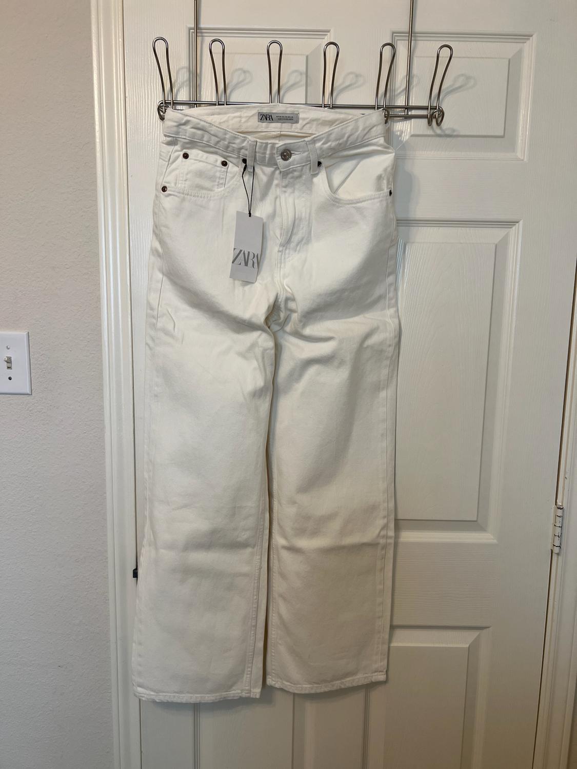 White denim trousers hanging on a clothes rail over a white door. They have a label bearing the text ZARA.