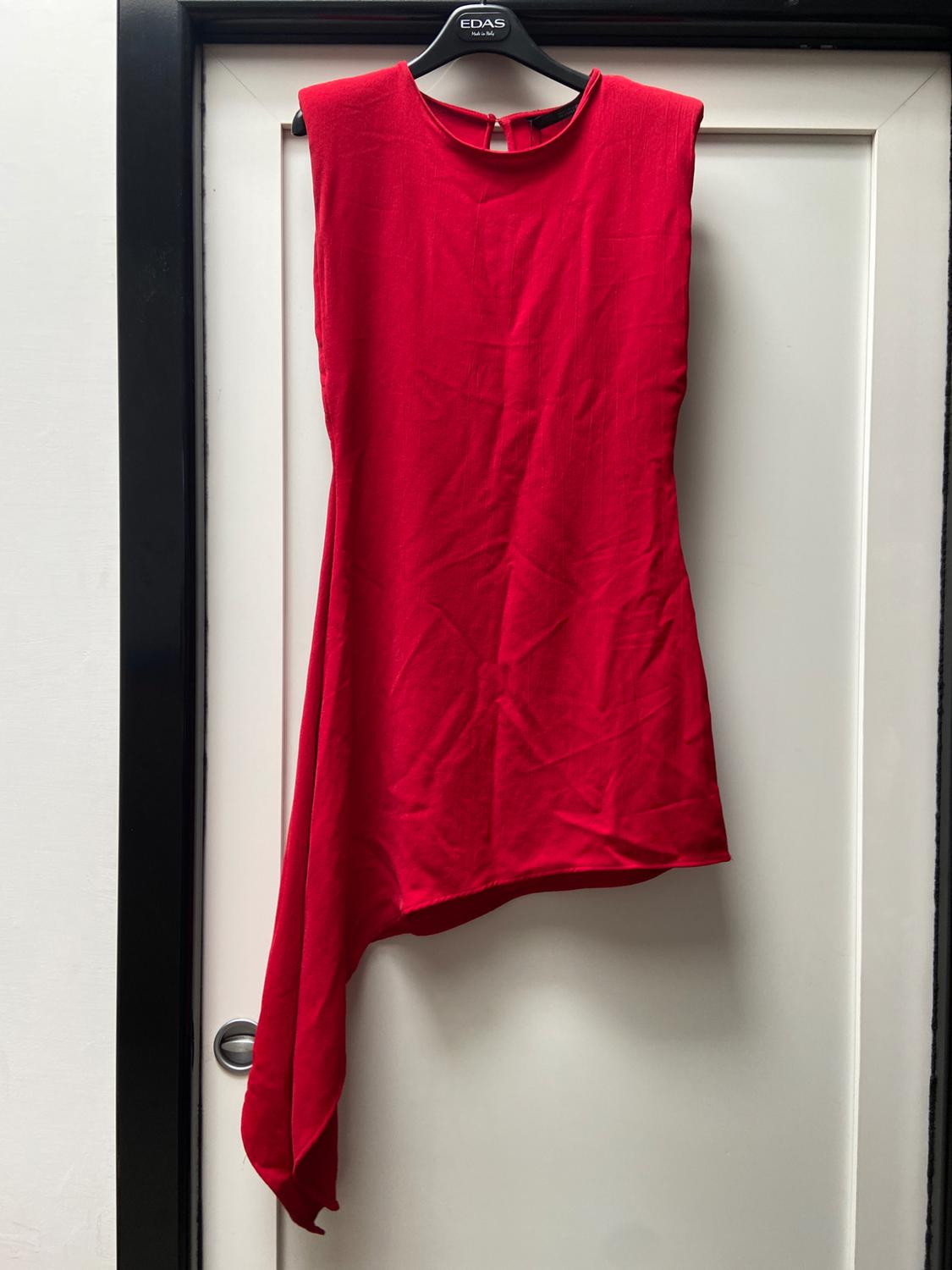 Red sleeveless dress with an asymmetrical hem hanging from a black coat hanger on a white door. Visible text: EDAS.