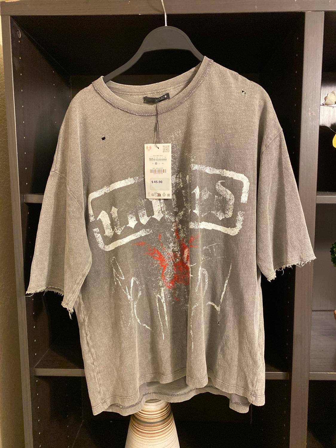 Worn grey t-shirt with white and red print, hanging on a black hanger. Price tag of $45.90 visible.