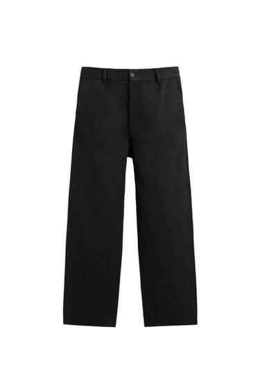 Front view of black regular fit trousers with elasticated waistband, front and back welt pockets, zip and button fastening.