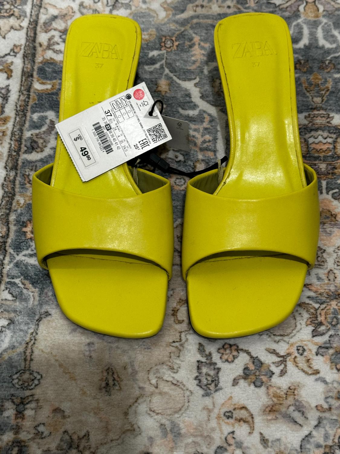 Yellow low-heeled sandals with a price tag of £49.90 on a floral patterned rug. Visible brand: ZARA. Size 37.
