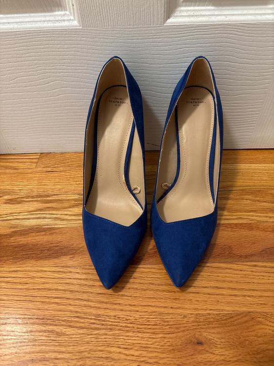 Dark blue high heels with a pointed toe on a wooden floor. Visible text: "Zara Trafaluc 38 1/2".