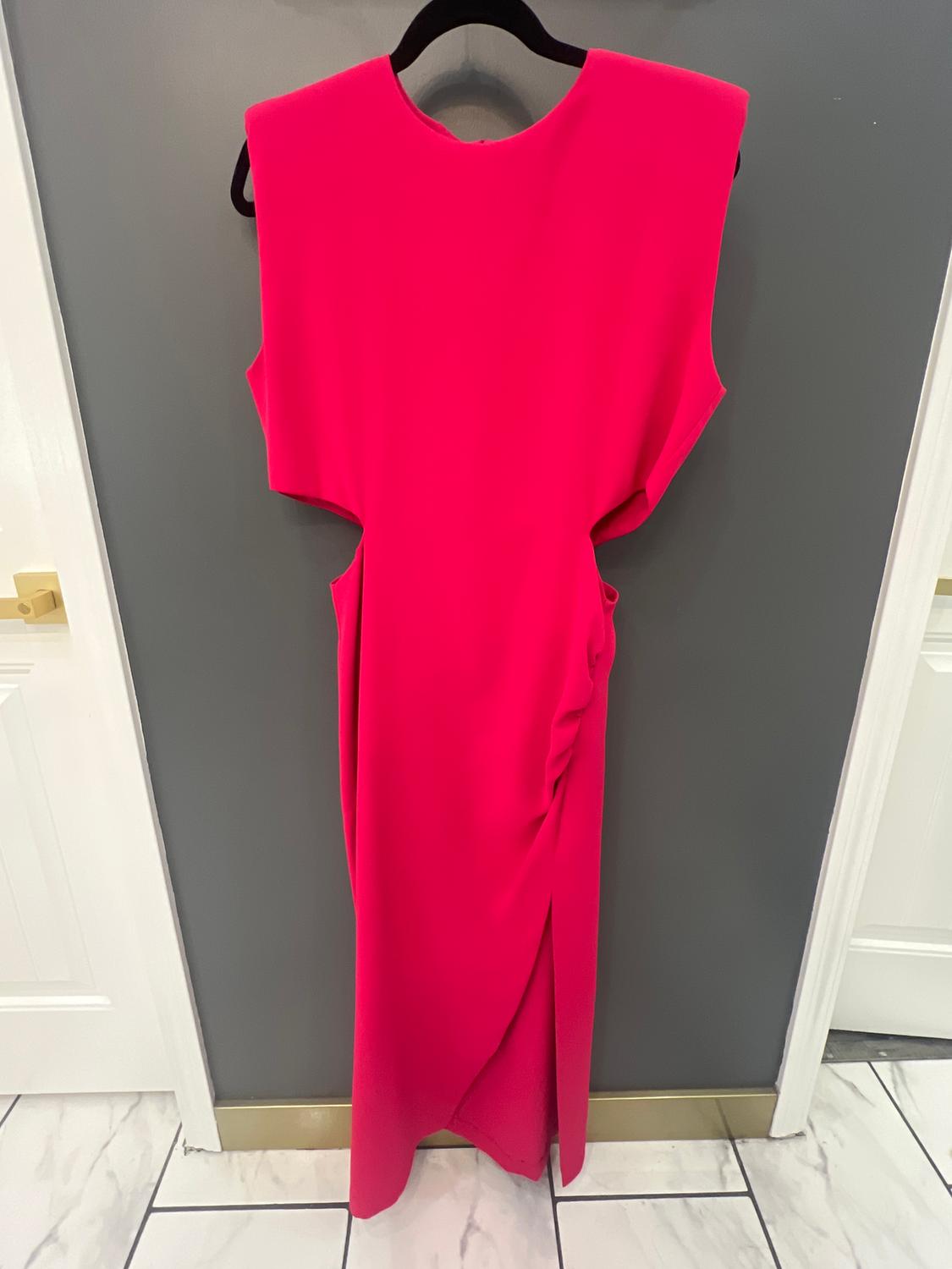 Fuchsia sleeveless dress with side slits, hanging on a black hanger against a gray wall. White tiled floor.