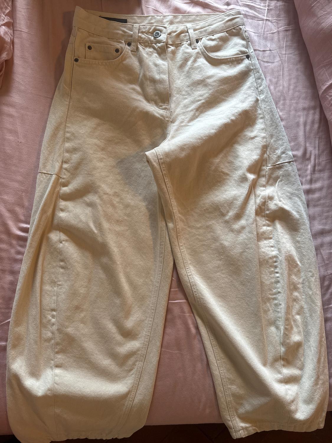 Cream-coloured wide-leg trousers with front seams, laid out on a wrinkled pink sheet, conveying a casual and relaxed style.