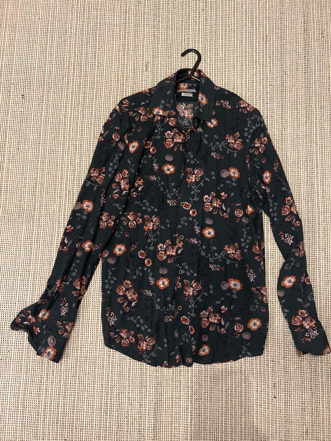 Dark and orange floral print long-sleeved shirt, hanging on a hanger against a beige fabric background.
