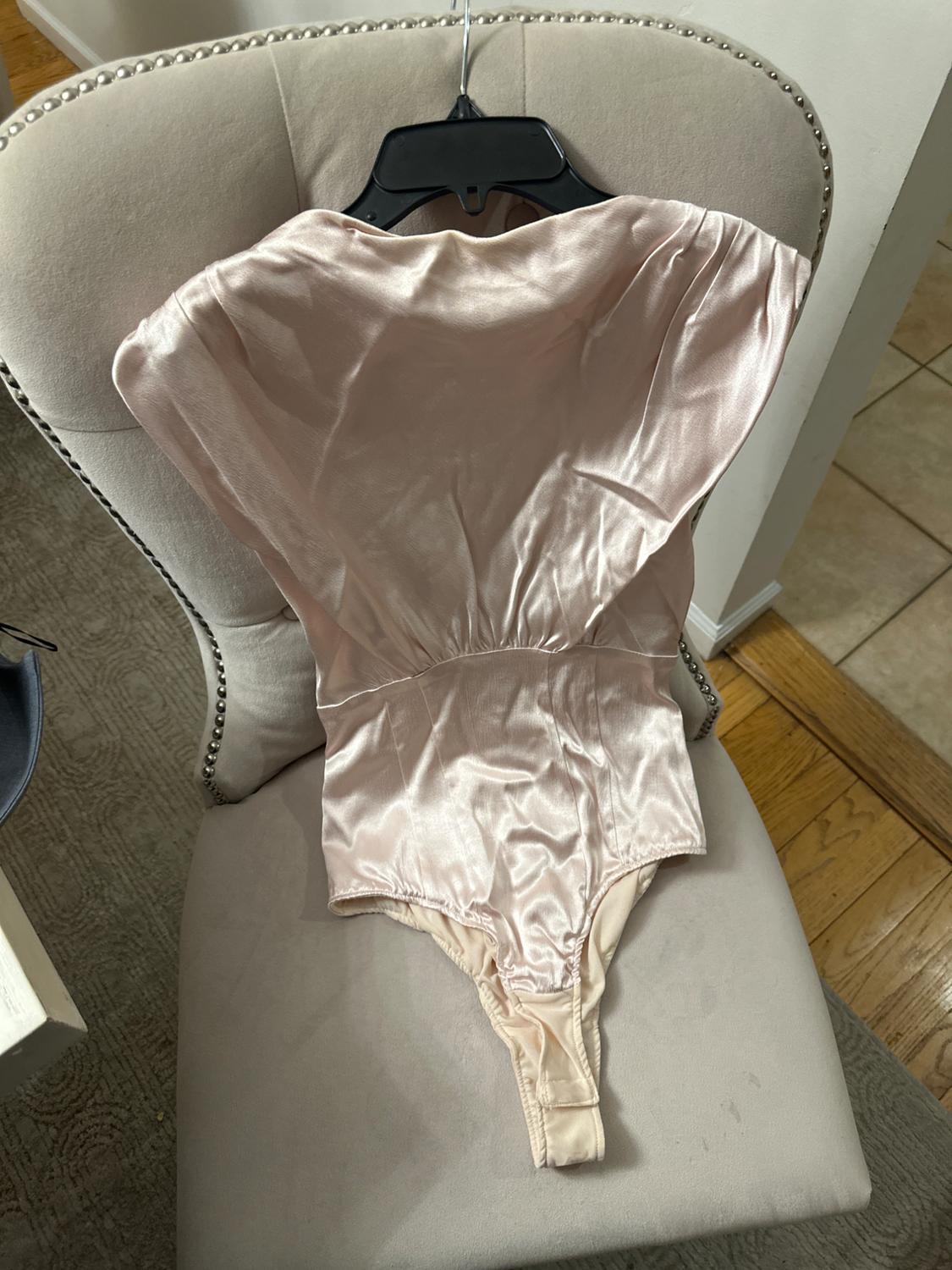 Front view of a light pink bodysuit with a shiny texture and a crotch opening.