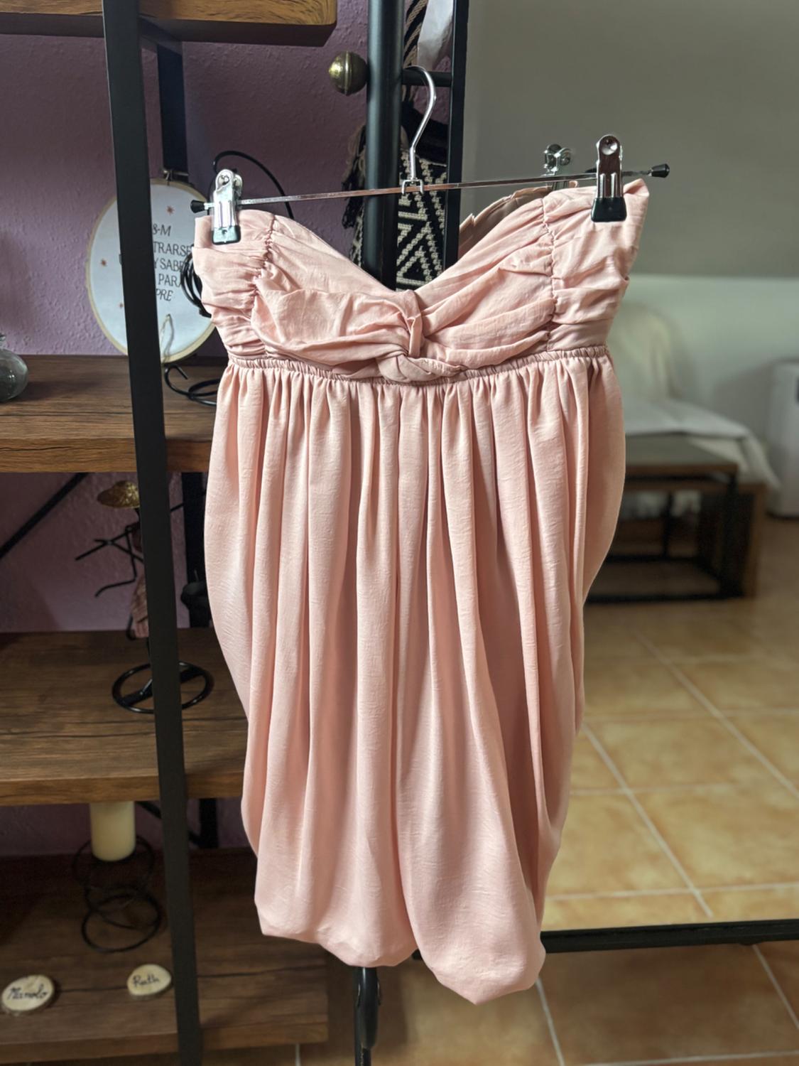 Strapless pink dress hanging on a hanger, with a wooden bookshelf and lilac wall in the background.