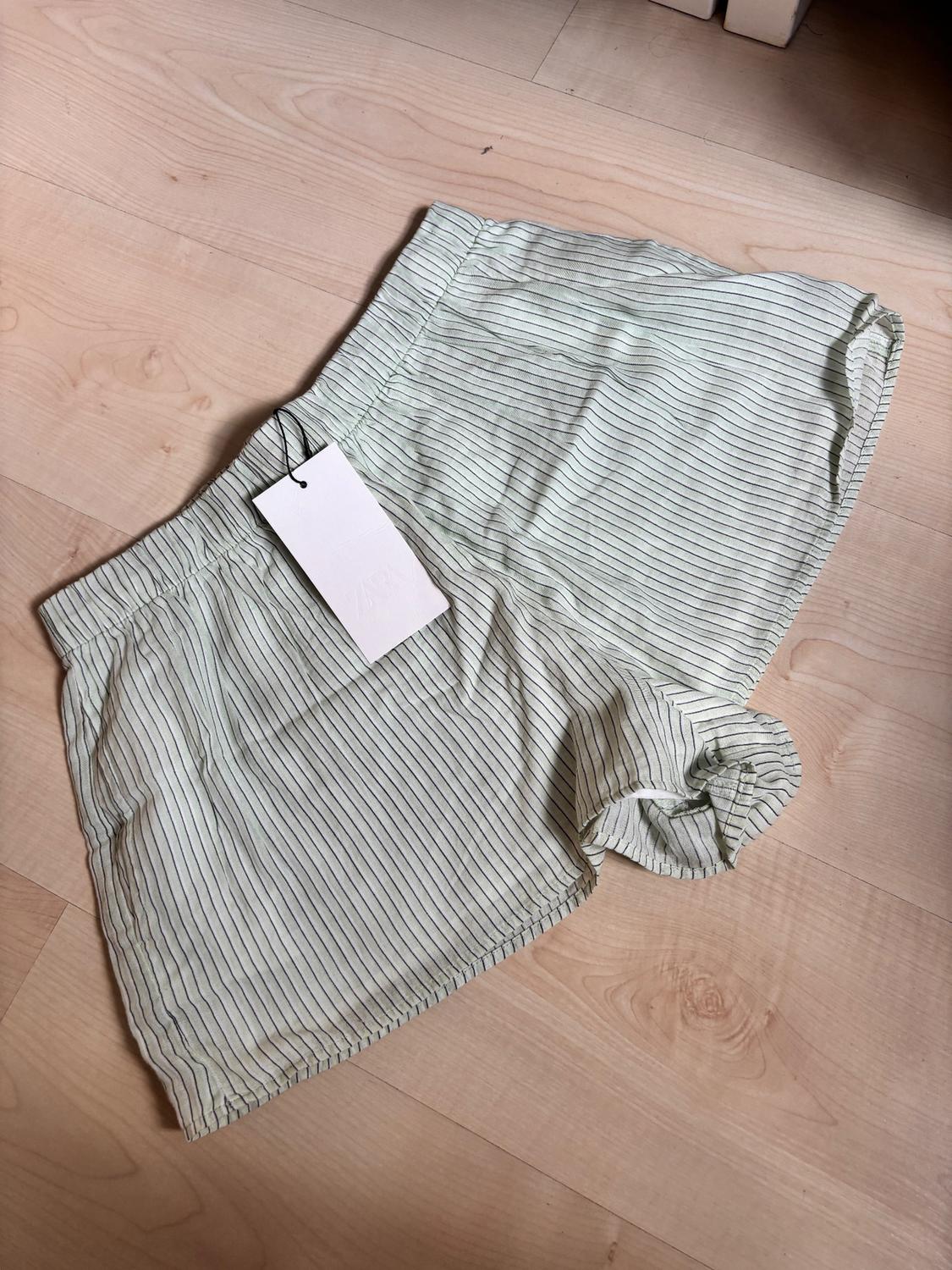 Black and white pinstripe shorts on a light wooden floor, with a white hanging tag.
