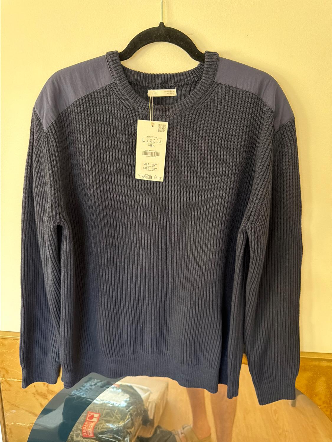 Dark blue, chunky knit jumper with shoulder detailing, hanging on a black hanger. Visible price and size tag.
