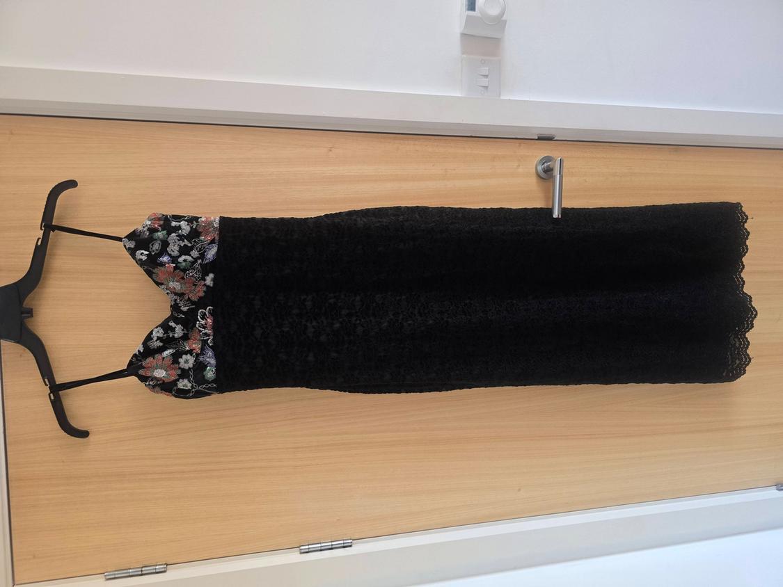 Black lace dress hanging on a wooden door, with thin straps and floral details on the top.